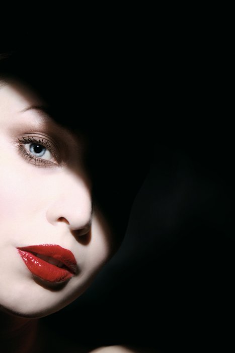 Портрет женщины с белым макияжем, красными губами и тенью на лице, снятый при жестком свете