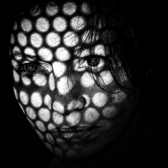 Портрет женщины с узорчатой сеткой света и тени, освещающей части лица