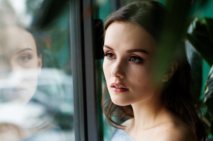 Портрет женщины с ее отражением в окне, демонстрирующий естественное освещение фотографии