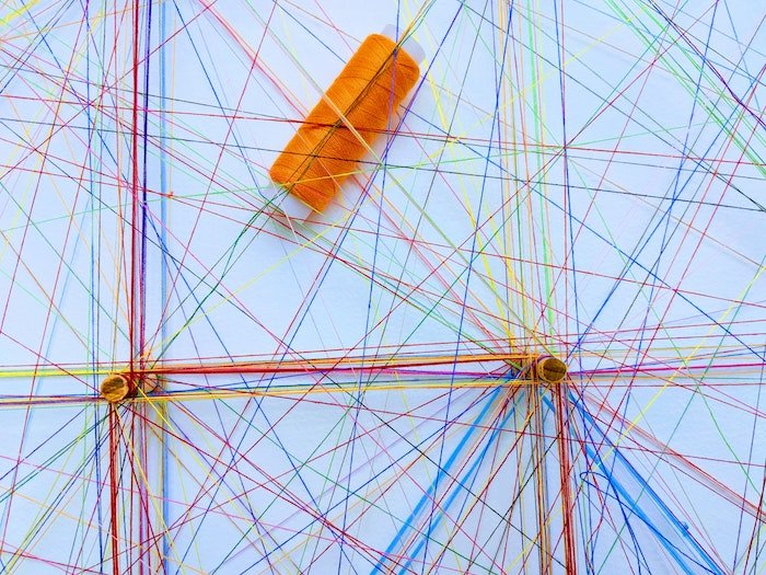 Катушка оранжевой нити на поверхности с переплетенными и пересекающимися в разных направлениях нитями цветной нити