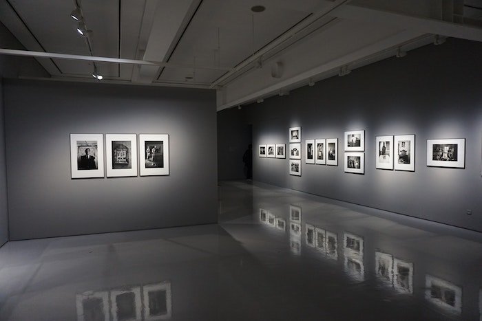 Пространство художественной галереи с серыми стенами и фотографиями в белых рамках на стене в точечных светильниках