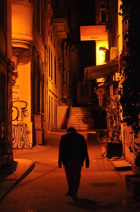 Уличная фотография в стиле raw, изображающая темный силуэт в пустом переулке с опущенными руками с красным и оранжевым освещением