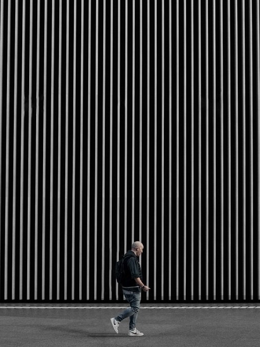 Мужчина идет у большой стены с тонкими графическими белыми линиями на черном фоне