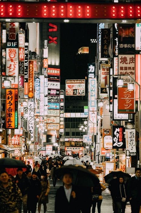 Люди с зонтиками идут по пешеходной улице в Японии, заполненной вывесками магазинов ночью
