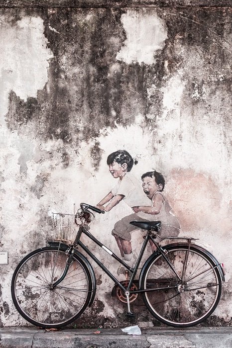 Черно-белая уличная фотография двух детей, сидящих на велосипеде у стены и смеющихся