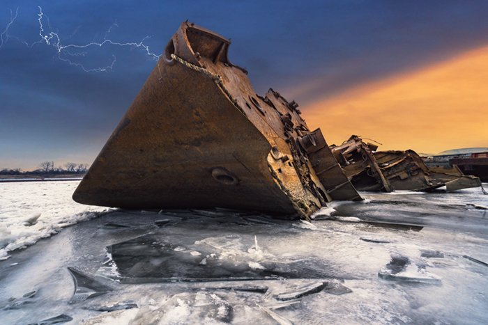 Rusted shipwreck on ice water with lightning in the sky