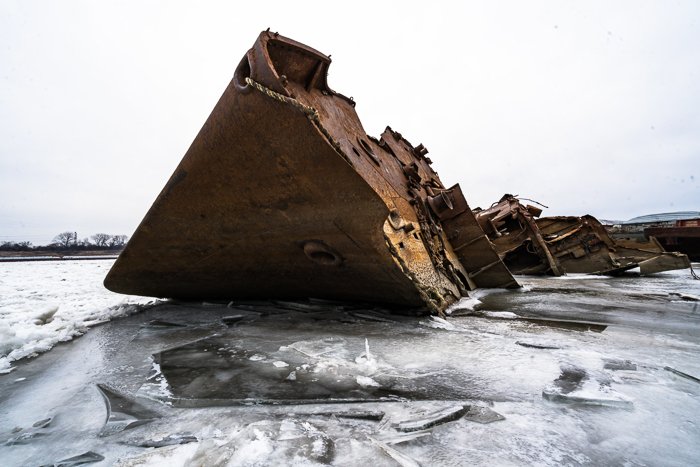 Rusted shipwreck on ice water with cloudy washed out sky