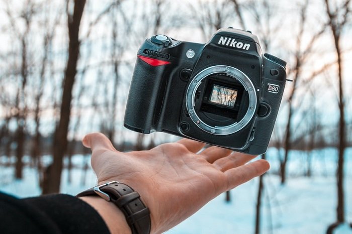 фотограф осторожно подбрасывает в воздух камеру Nikon под вытянутой рукой