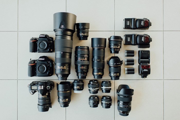 ряд фотокамер Nikon, объективов и вспышек, разложенных на кафельном полу