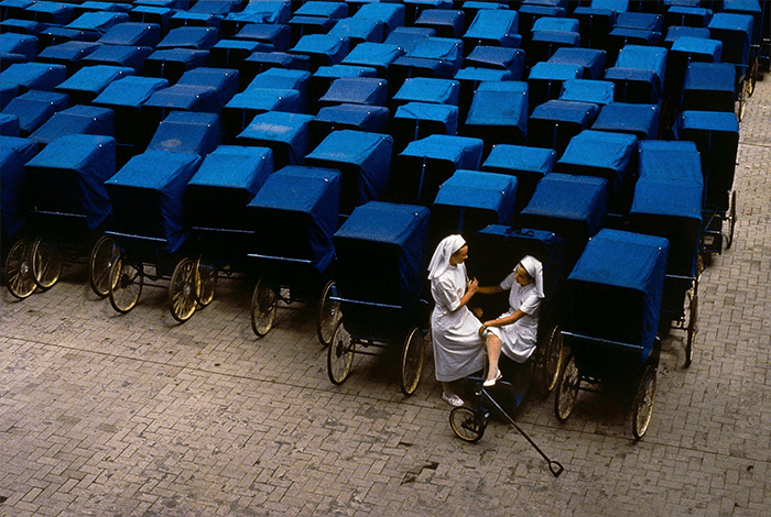 Разрыв шаблона в фотографии: изображение двух медсестер, сидящих среди множества синих рикш от Стива МакКерри